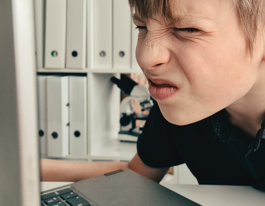 Niño entrecerrando los ojos, con dificultad para ver la pantalla de su laptop