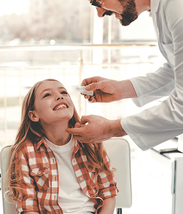 Doctor aplicando gota para los ojos a niña sonriente de 10 años