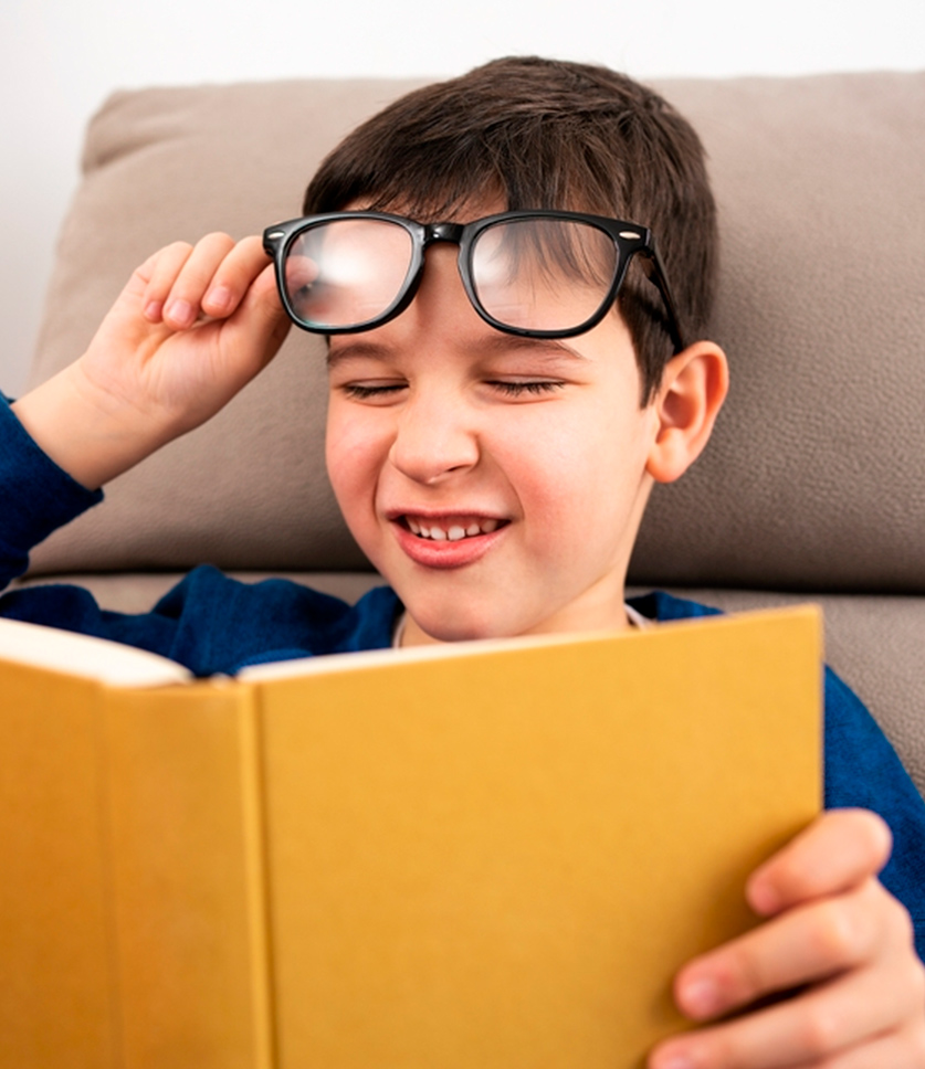 Niño con lentes tratando de leer con dificultad un libro
