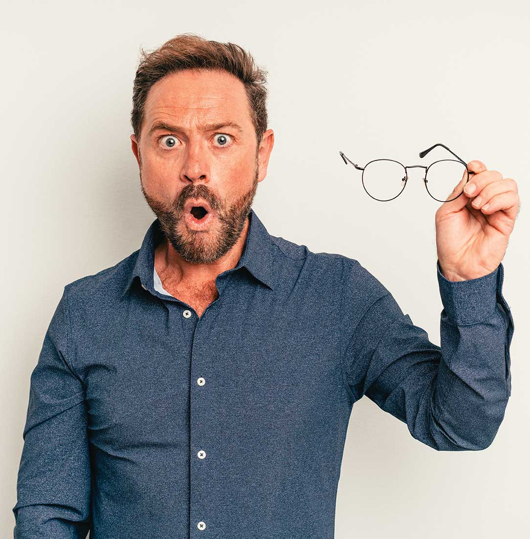 Hombre sosteniendo unos lentes óptimos en su mano con expresión sorprendida