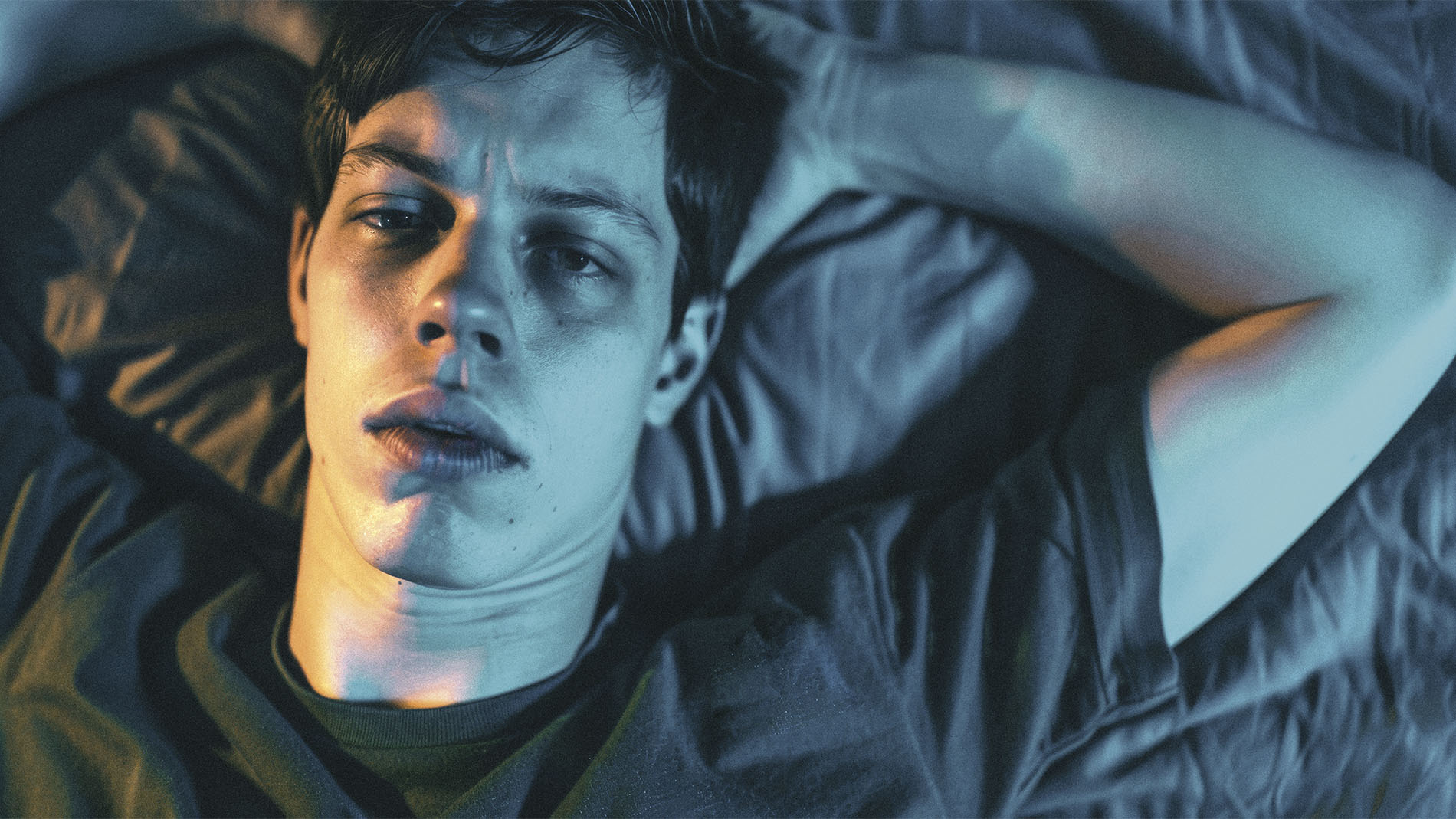 Retrato de hombre joven acostado en su cama, luciendo cansado y con los ojos ligeramente abiertos, ejemplificando la relación entre la salud mental y la oftalmología