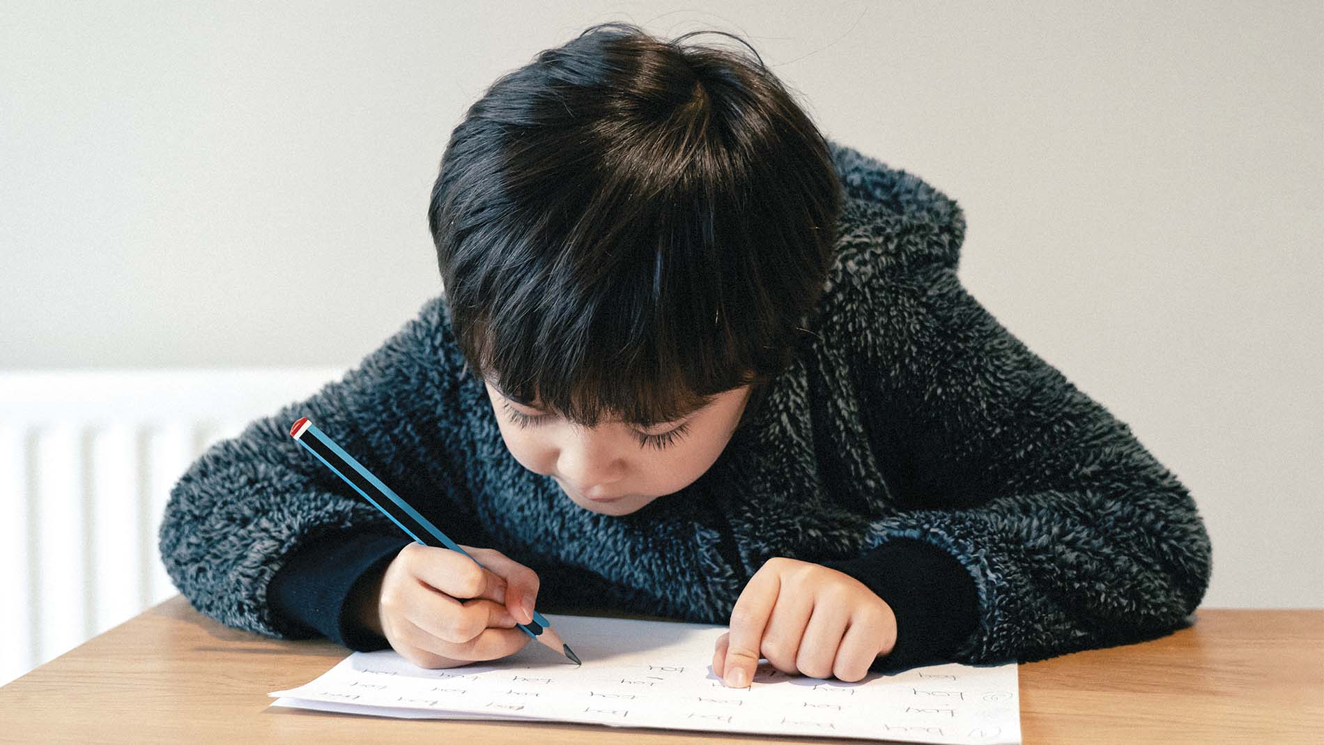 Niño haciendo tarea escolar apoyado sobre mesa de madera