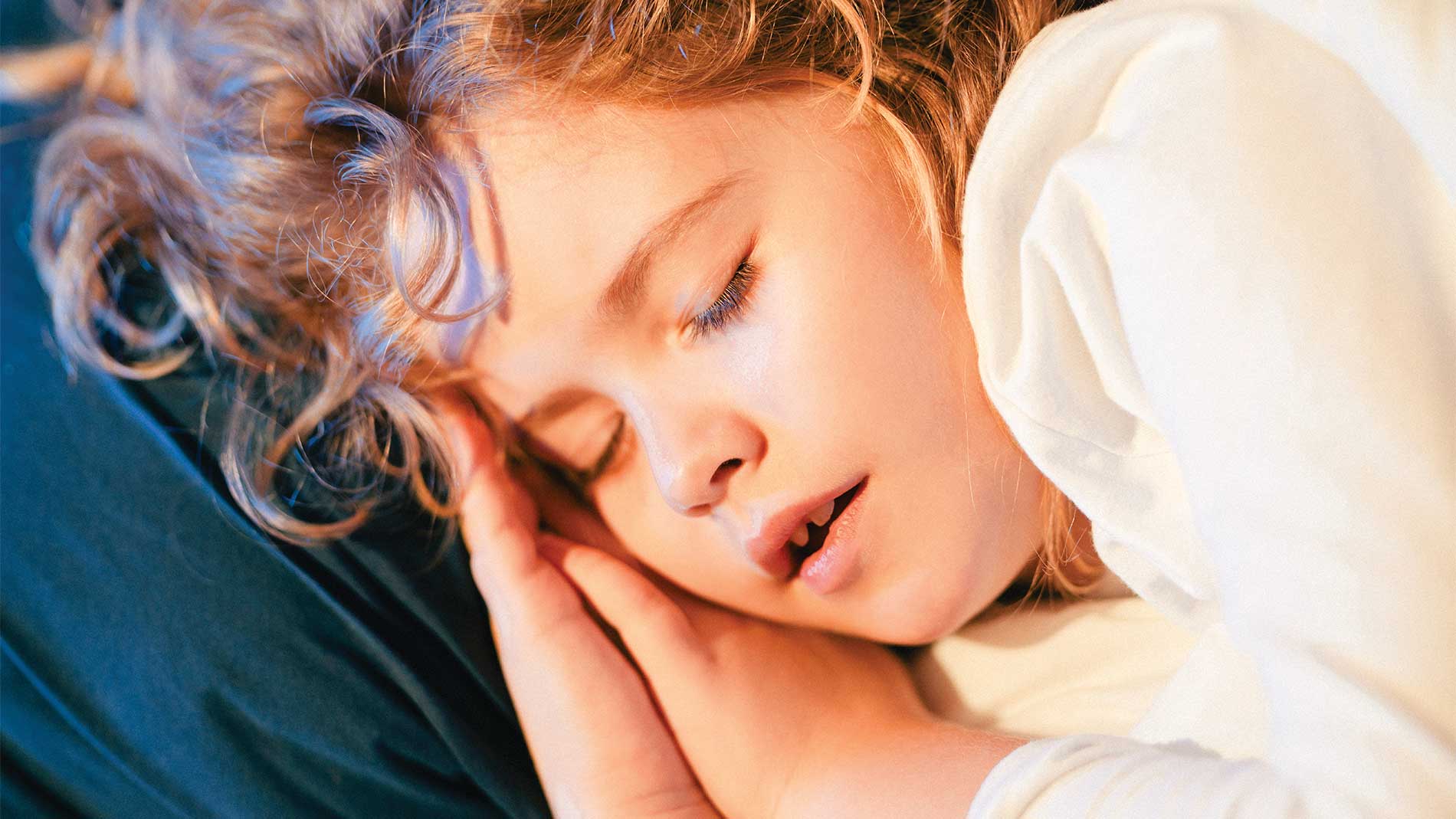 Niña durmiendo con las manos debajo de la cabeza, recargada sobre una almohada color azul
