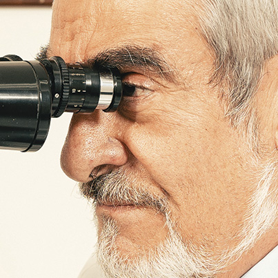 Retrato de Dr. Federico Graue Wiechers viendo a través de aparato para estudio de la vista