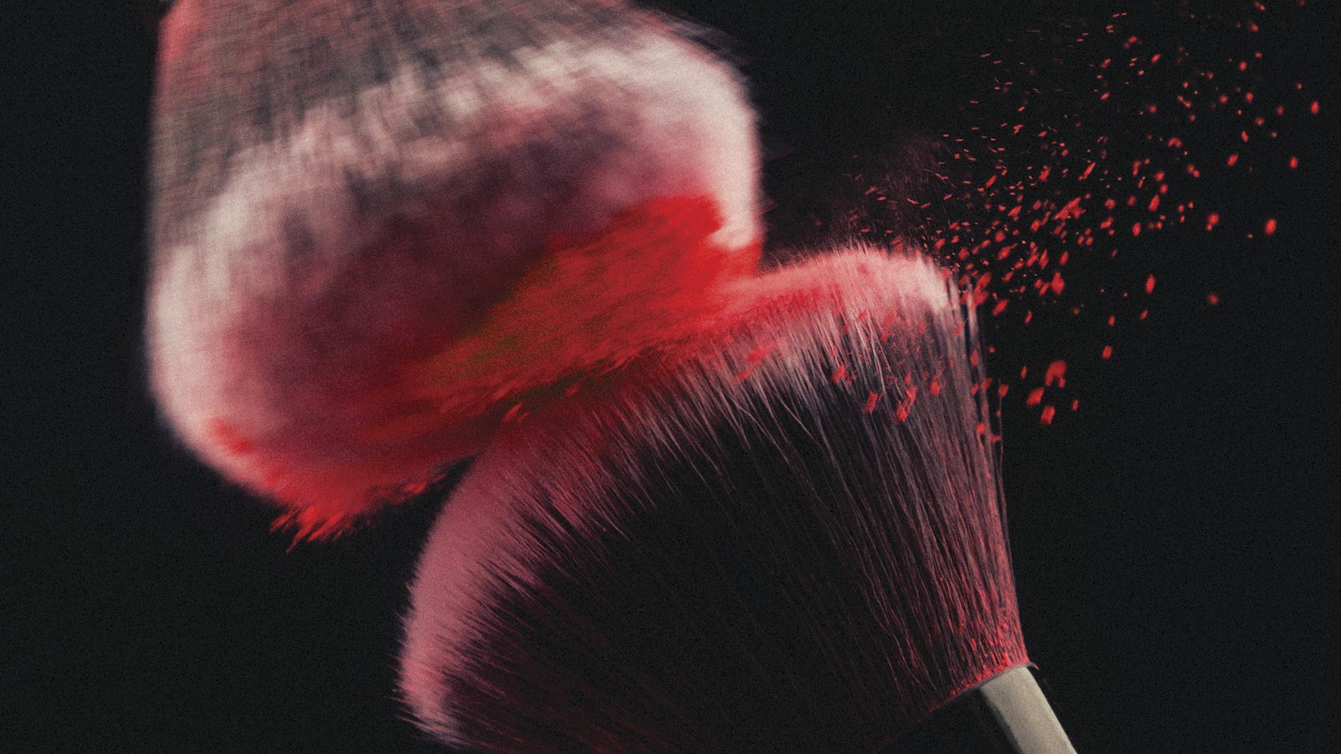 Dos brochas para aplicar cosméticos cubiertas con maquillaje rojo sobre fondo negro