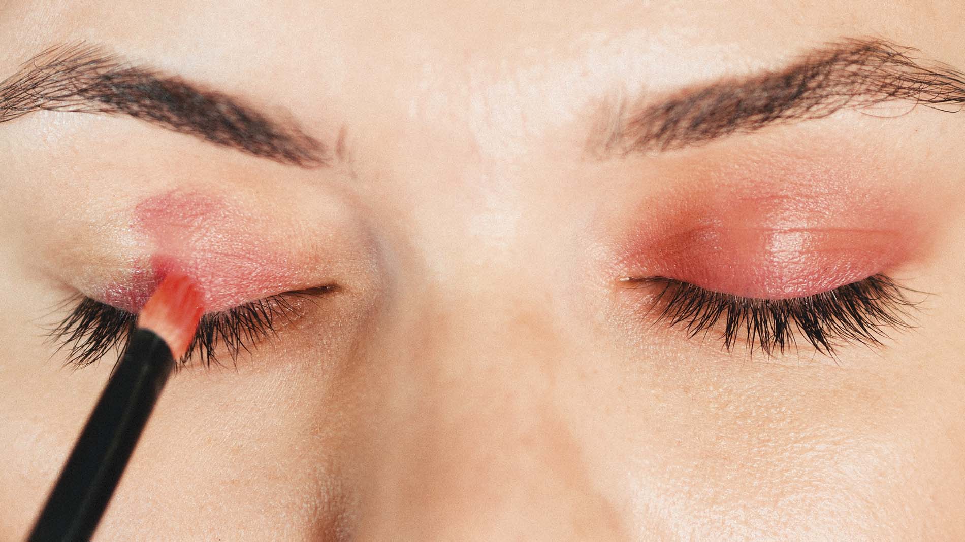 mujer aplicando cosméticos color rojo con una brocha sobre párpados cerrados