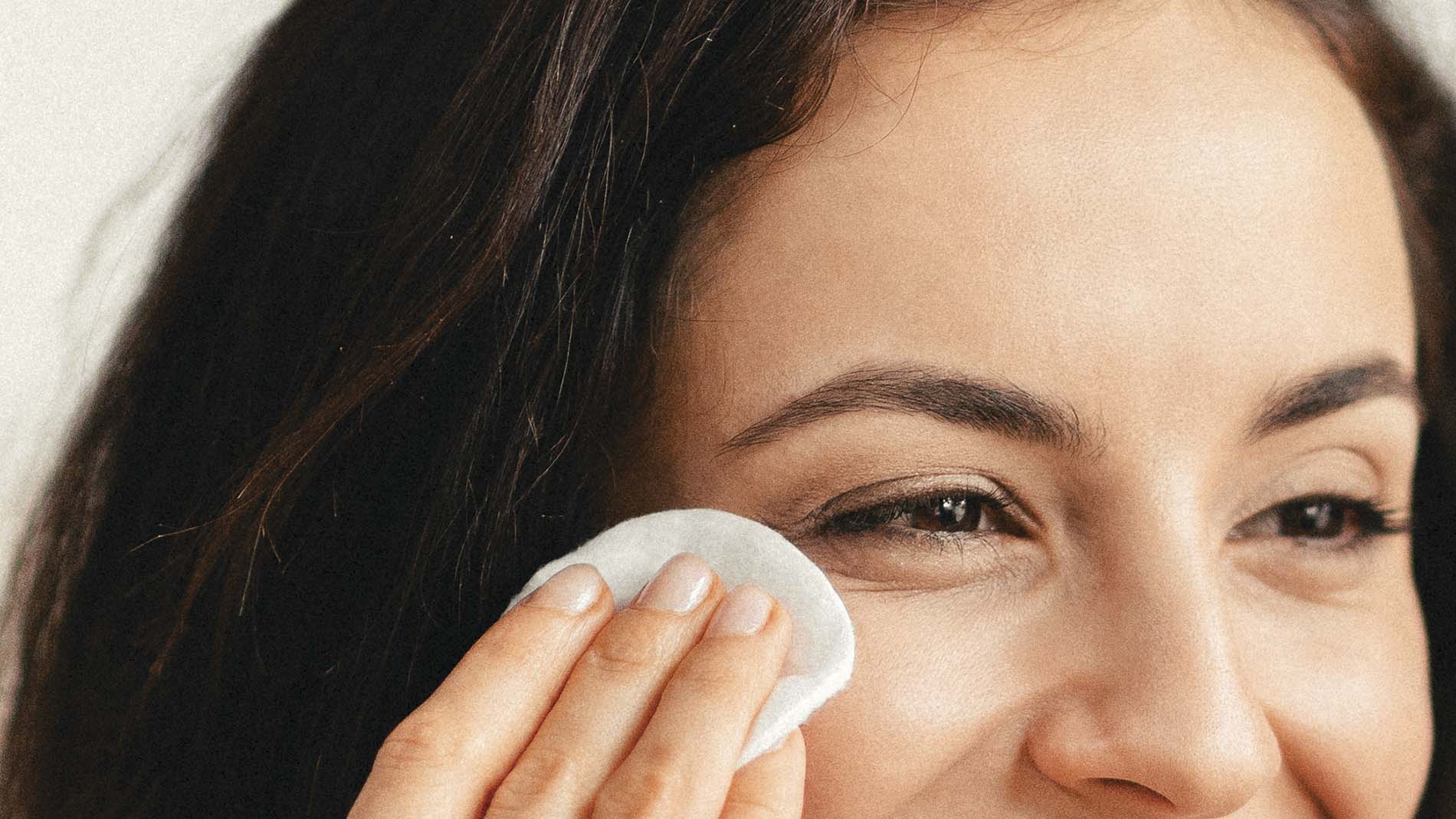 mujer sonriente usando almohadilla de algodón para quitar cosméticos