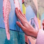 Mano de mujer tocando una obra de arte de color rosa, azul y verde