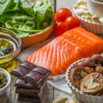 Alimentos variados que aportan nutrición para los ojos (salmón, aguacate, aceite de oliva, nueces, espinacas, chocolate y otros) acomodados sobre una mesa de madera