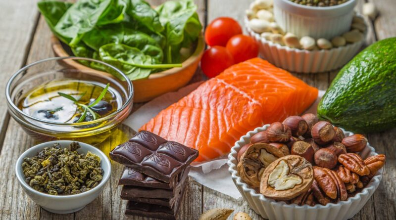 Alimentos variados que aportan nutrición para los ojos (salmón, aguacate, aceite de oliva, nueces, espinacas, chocolate y otros) acomodados sobre una mesa de madera