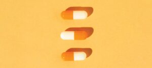 tres cápsulas de medicina alineadas verticalmente sobre fondo anaranjado, representando medicina para el tratamiento del ojo seco