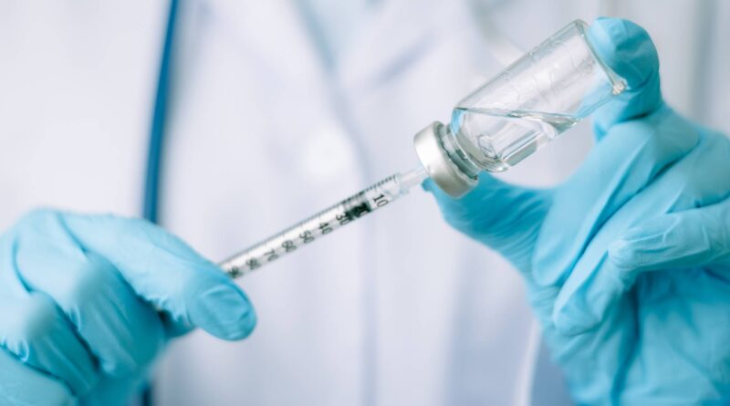 Manos de un médico usando guantes de latex azul sosteniendo con la mano derecha una jeringa y con la mano izquierda una ampolleta que contiene medicamento para enfermedad de los ojos