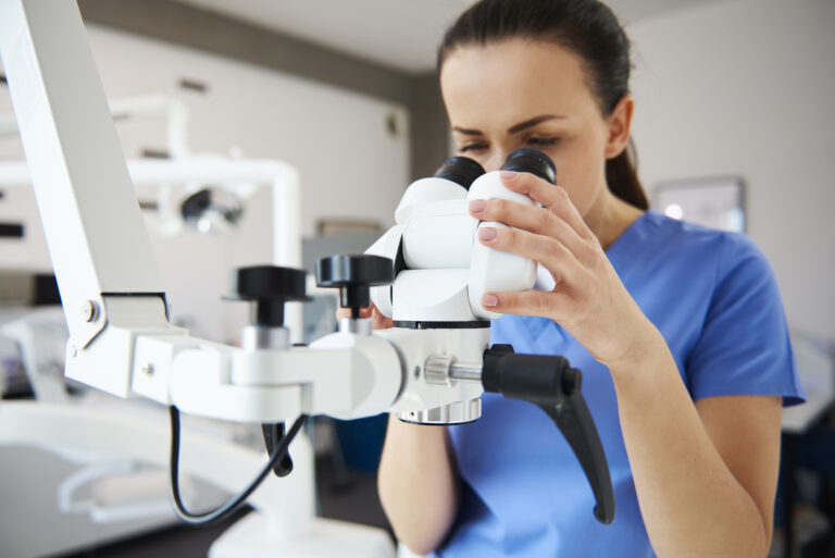 Mujer especialista observa a través de un microscopio clínico, en una sala equipada para procedimientos oftalmológicos y diagnóstico ocular avanzado.