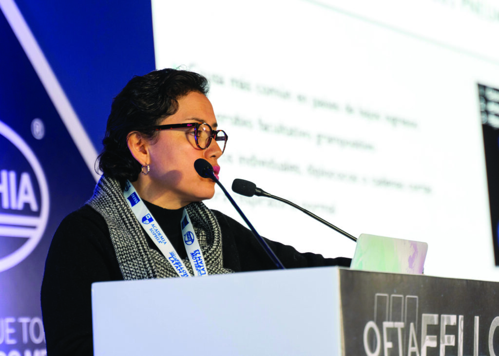 Doctora oftalmóloga, Elisa Alegría Gómez, hablando por micrófono en un podio durante su conferencia en el evento Oftafellow 2023
