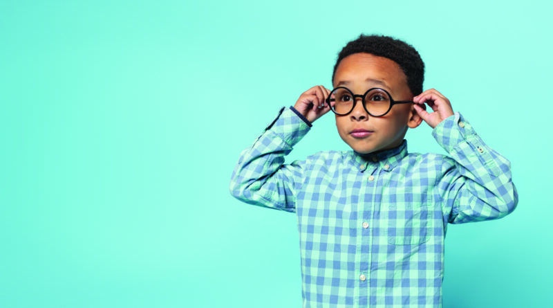 Niño afroamericano con deficiencia visual usando lentes con graduación, posando en un estudio con fondo color azul. En el contexto de los avances en oftalmología con una visión global
